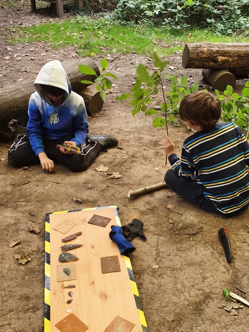Two children sitting in the woods examining bushcraft tools and natural materials