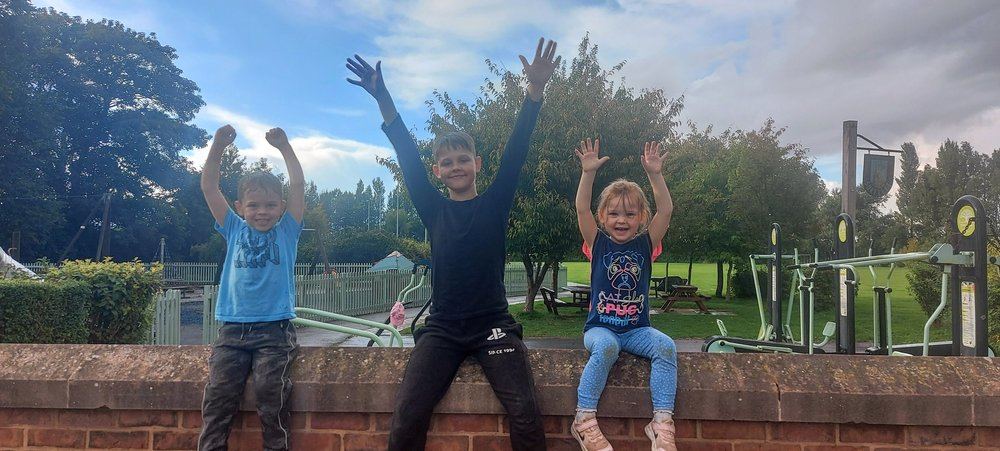 Three children cheering with their hands raised at a park