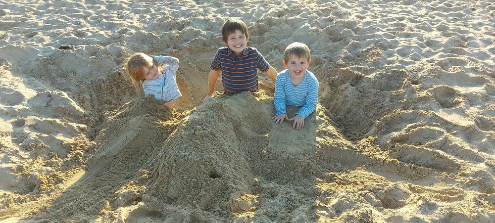 Three children playing together, digging in the sand at the beach